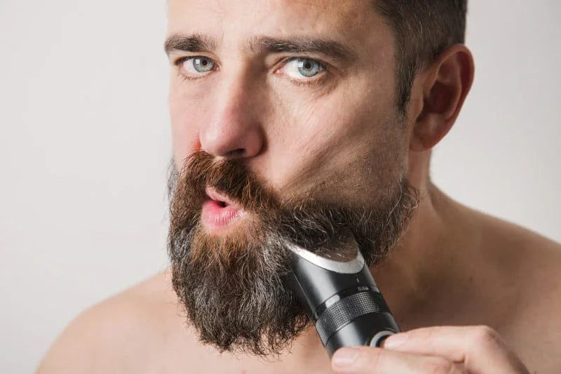 Man trimming thick beard with electric beard trimmer close up